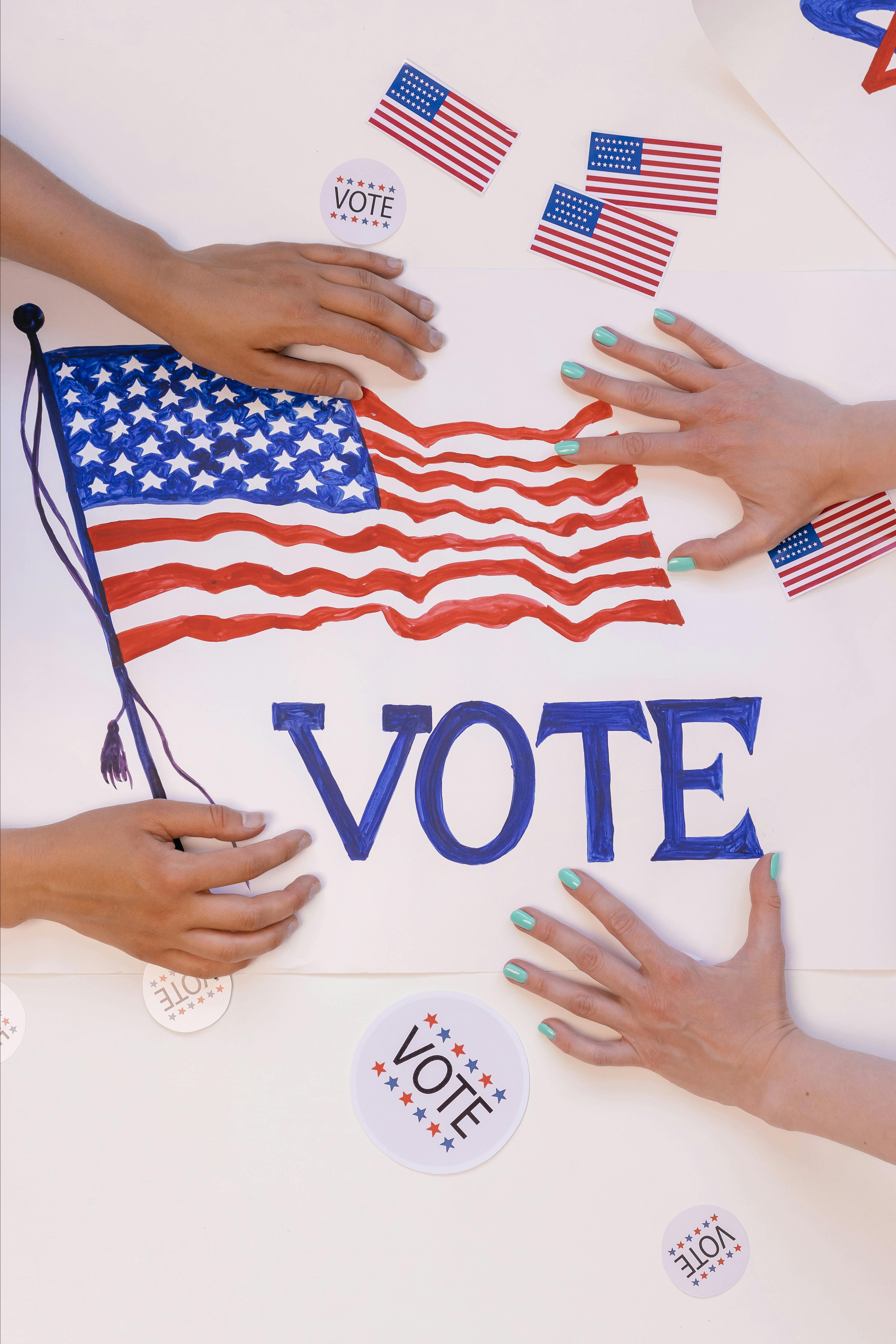 An waving American flag surrounded by small flags and the word Vote with hands surrounding the flag